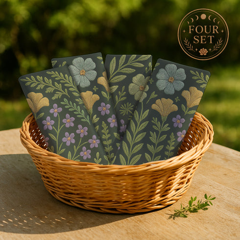 A 4-piece cloth napkin set featuring embroidered-style botanical illustrations of wildflowers and herbs in shades of gold, mint, and lavender on a dark green background; made from soft polyester, square-shaped, with a luxe and mystical design.